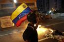 An opposition demonstrator carries a Venezuelan flag as he walks past a burning barricade during a protest in Caracas