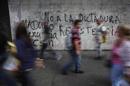 Pedestrians walk past a wall covered with graffiti at the district of Chacao in Caracas