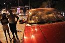 People stand near a SUV vehicle with a broken windshield after protesters threw stones at the driver in Caracas