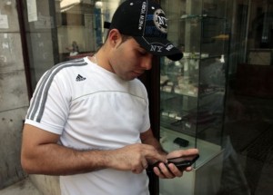 A young Cuban man wearing a New York cap and an Adidas T-shirt using a cell-phone in Havana. Credit: Jorge Luis Baños/IPS