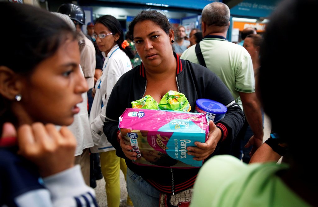  A woman holding food and other staple goods walks outside a supermarket in Caracas, Venezuela, June 30, 2016. REUTERS/Mariana Bazo 